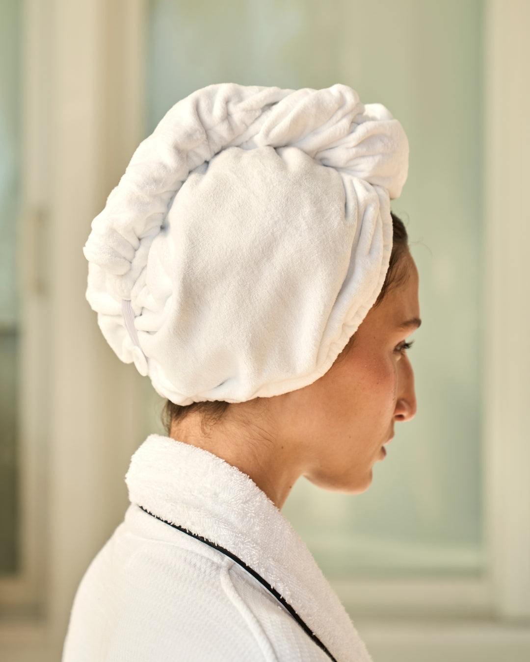 Woman wearing a white towel on her head in a neutral setting