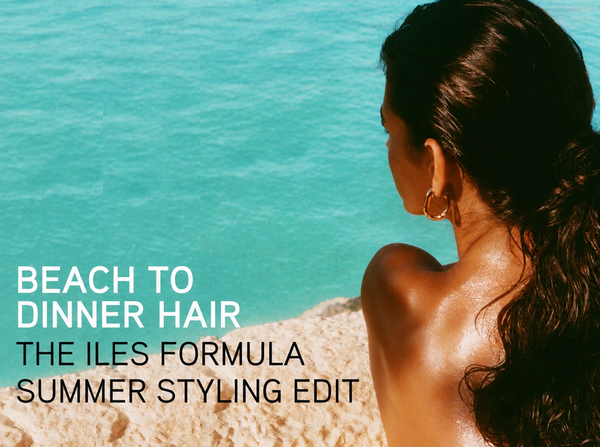Iles Formula "Beach to Dinner Hair" summer styling edit blog cover: woman seen from behind by turquoise blue sea with glossy dark wavy hair pulled back, a gold hoop earring, and sun-kissed skin.