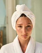 Woman wearing a white towel on her head and robe in a bathroom setting