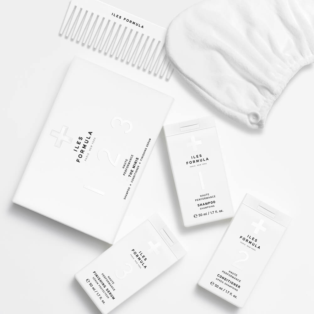 Flat lay of Iles Formula haircare set with shampoo, conditioner, finishing serum, a white comb, and a hair wrap, all arranged on a white background.