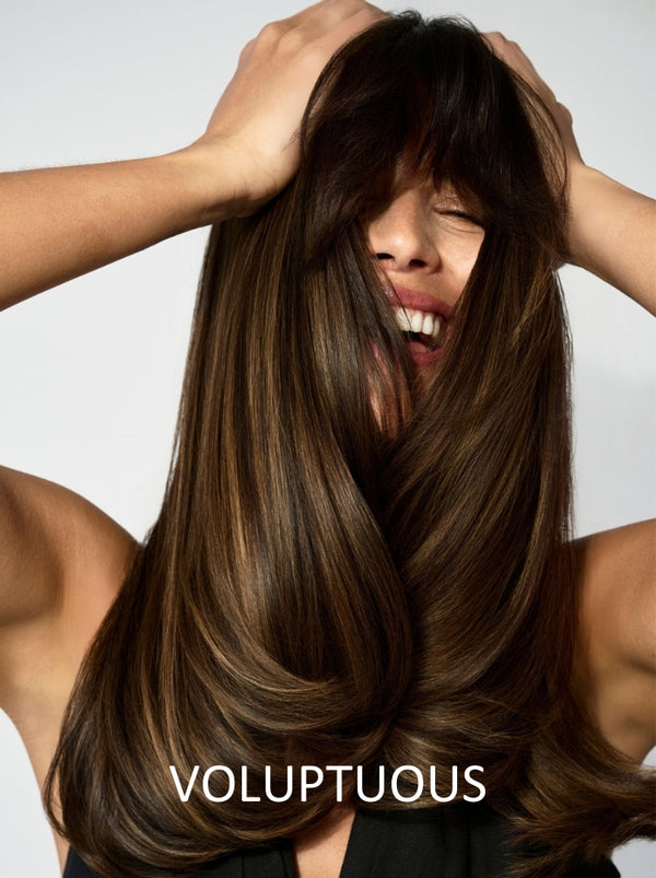 Woman with long, straight brown hair styled with bangs, posing against a neutral background.